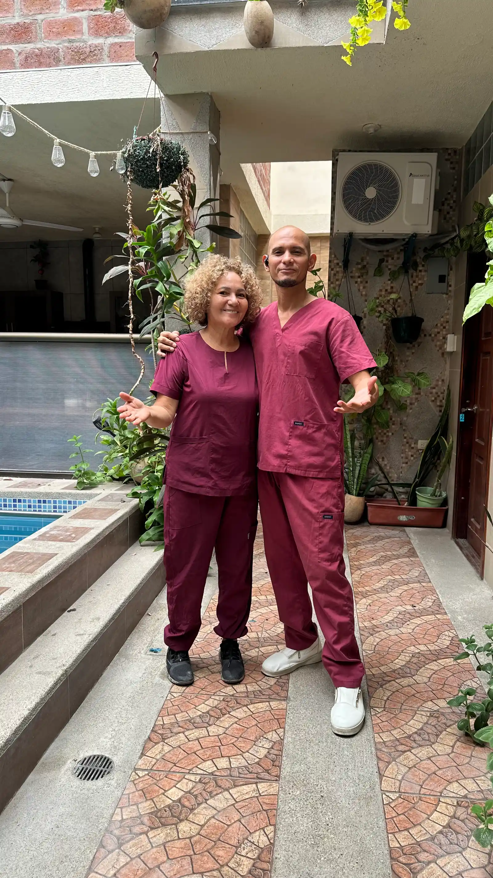 Two SIRONA team members in burgundy uniforms pose in a plant-filled hallway next to the pool.