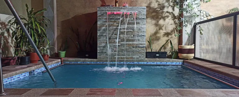 Indoor pool with a water cascade and surrounding plants.